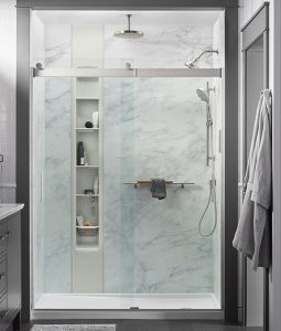 A stunning walk in shower with marble-pattern walls and built-in shelves.